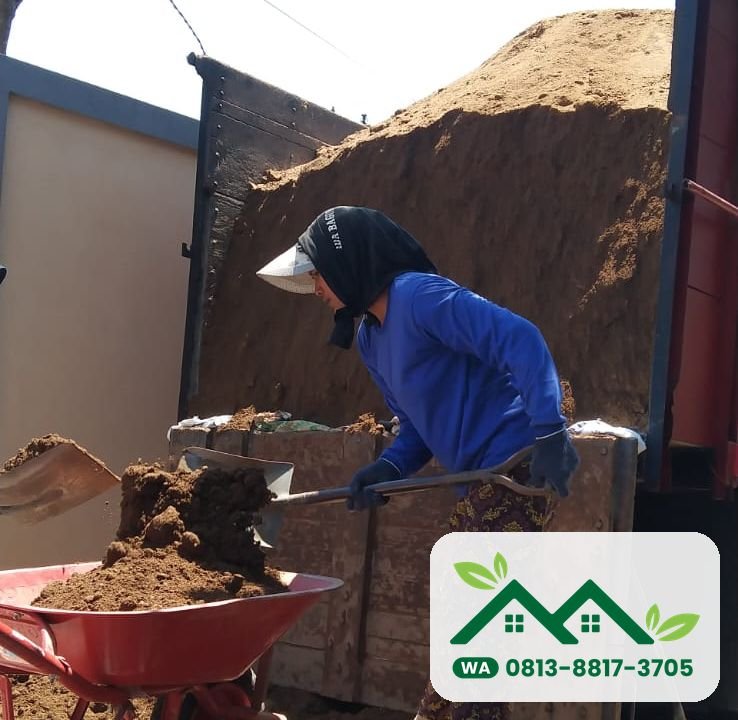 Pekerja menurunkan tanah subur dari truk bak kayu ke arco