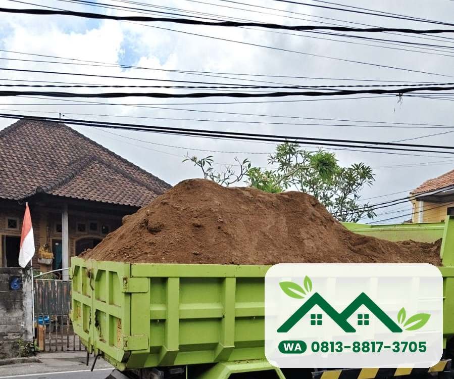 Dam truk hijau penuh tanah subur di jalan perumahan